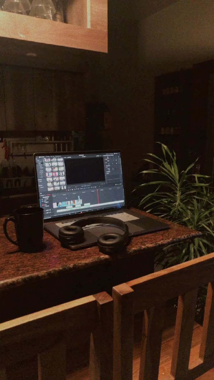 A laptop running an edit timeline late at night, headphones beside it